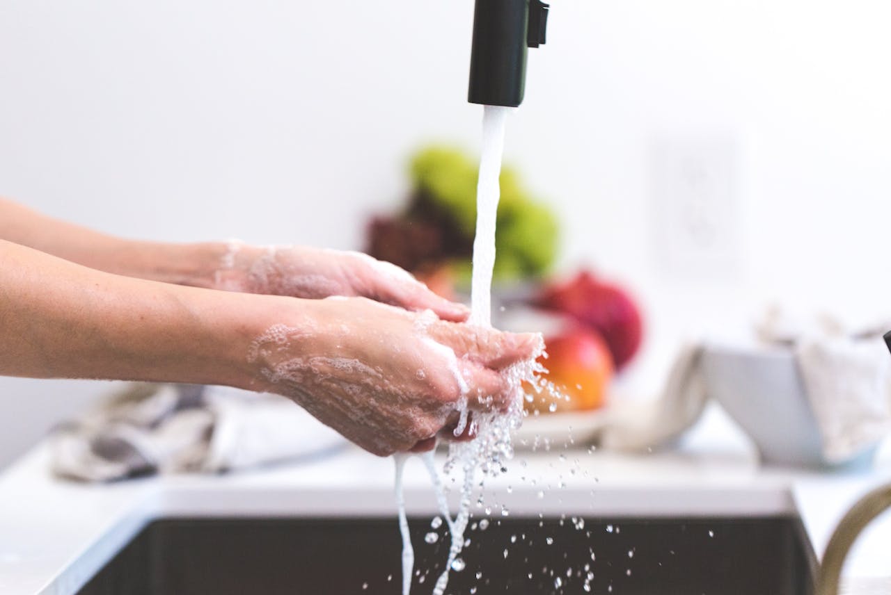 services-01 Hands being washed under a tap in a kitchen, promoting hygiene and cleanliness.